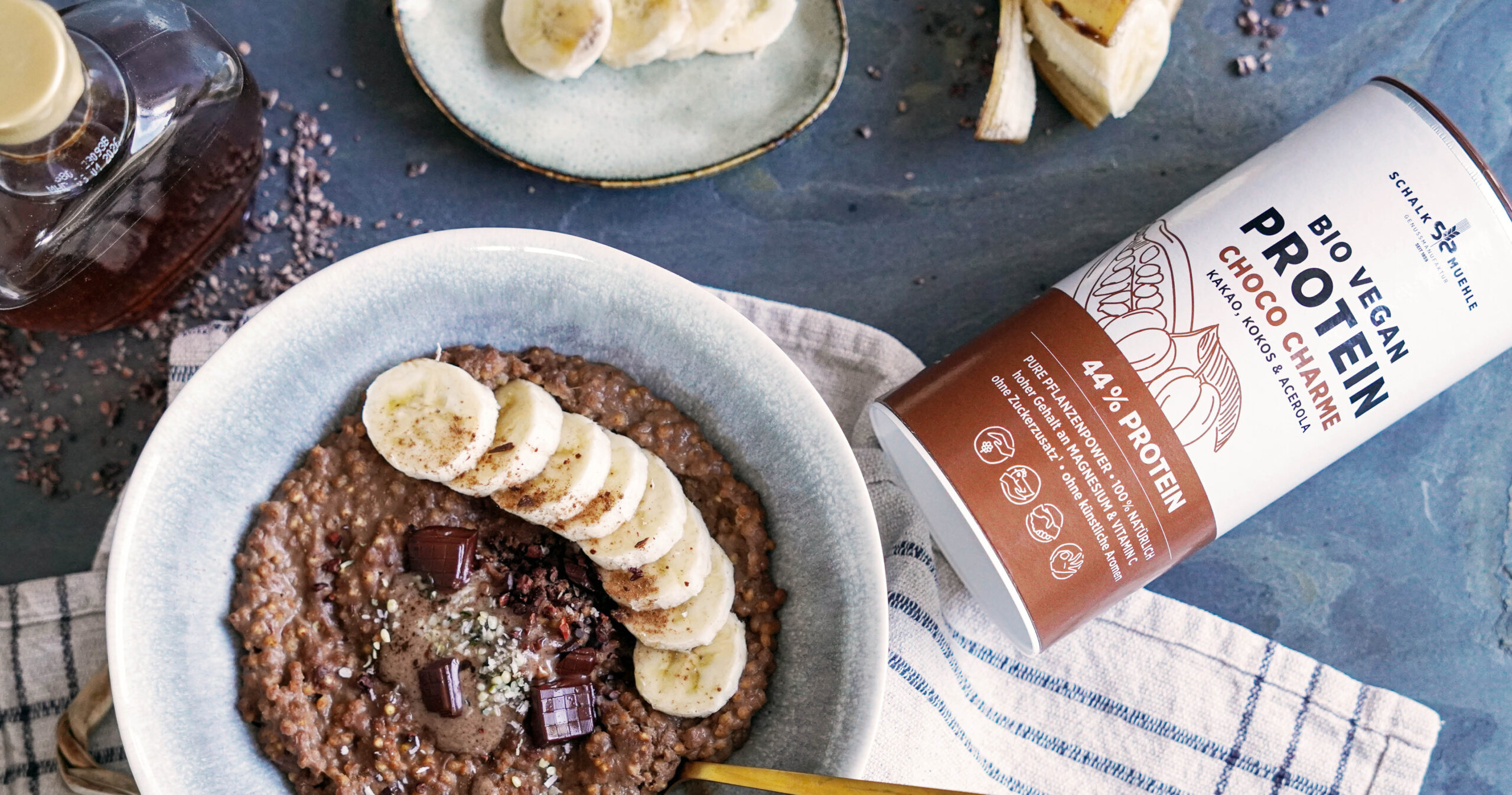 Schoko-Buchweizen-Porridge mit Bananen und Schokolade neben Schalk Mühle Bio Vegan Protein Choco Charme