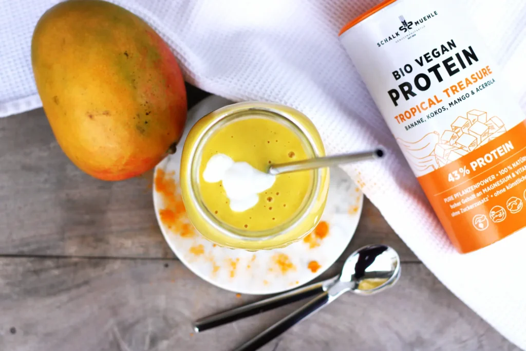Yellow mango lassi in a glass with mango and Schalk Mühle Organic Vegan Protein Tropical Treasure