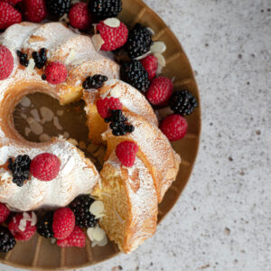 Gugelhupf mit Staubzucker, Himbeeren, Brombeeren und Mandelblättchen auf goldenem Teller