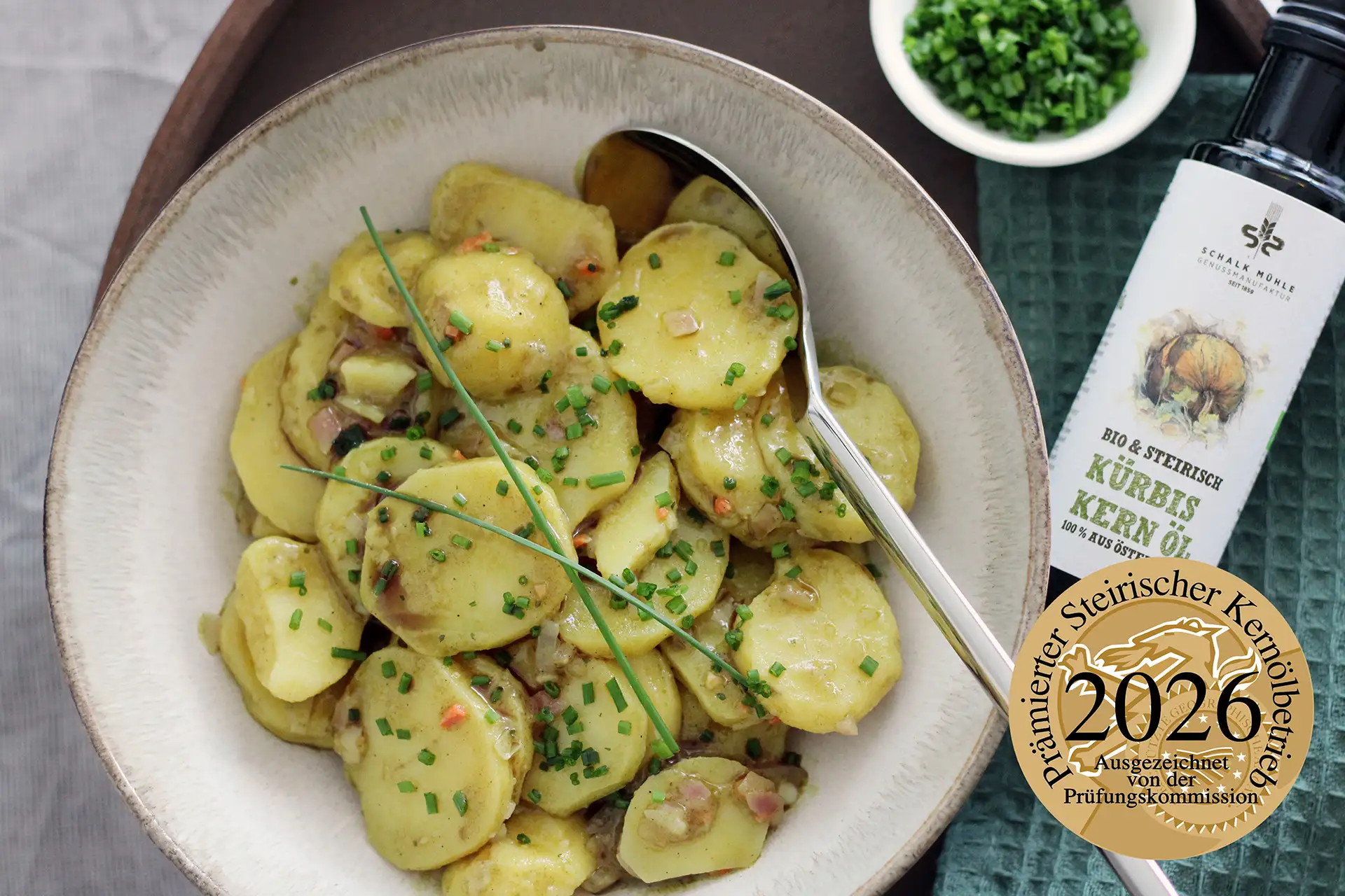 Steirischer Kartoffelsalat mit Schnittlauch und Schalk Mühle Kürbiskernöl, angerichtet in einer Schüssel