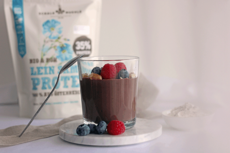 Schoko-Leinsamen-Pudding im Glas mit Himbeeren und Heidelbeeren, dahinter Schalk Mühle Leinsamen-Protein-Beutel