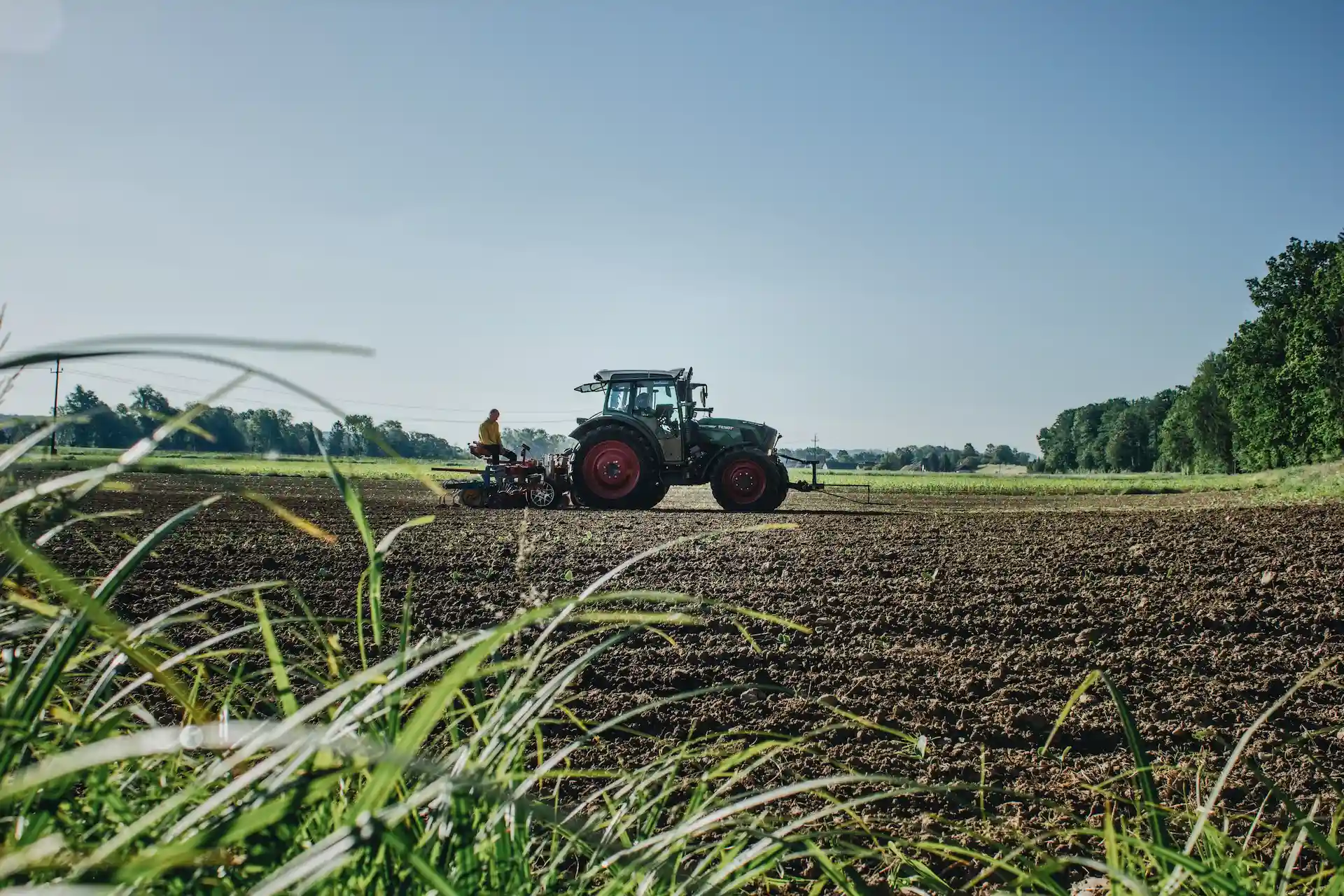 Tractor with implement during fieldwork on a freshly cultivated field under a blue sky