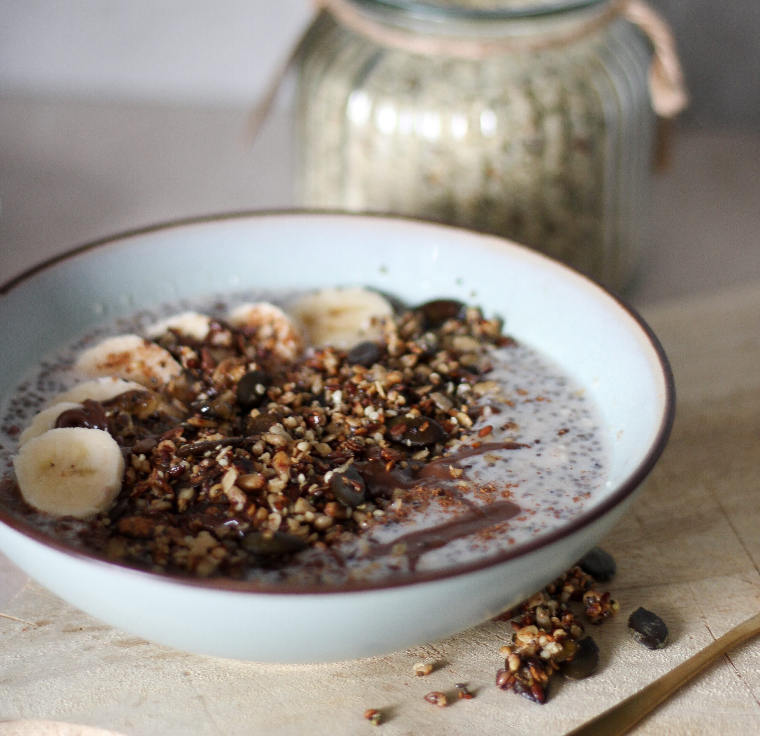 Chia-Pudding-Bowl mit Bananenscheiben, knusprigem Müsli und Schokosauce in heller Schale