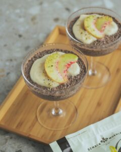 Zwei Gläser Chia-Pudding mit Vanillecreme und Pfirsichspalten auf einem Holztablett, daneben eine Schalk Mühle Packung