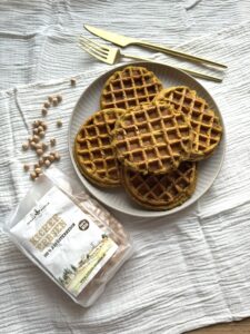 Goldene Kichererbsen-Waffeln auf Teller mit goldenem Besteck, daneben Schalk Mühle Kichererbsen
