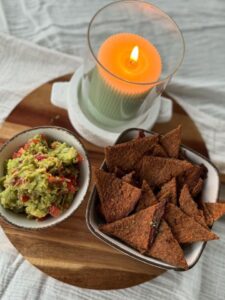 Knusprige Linsenchips mit Guacamole auf Holzbrett, daneben eine brennende Kerze