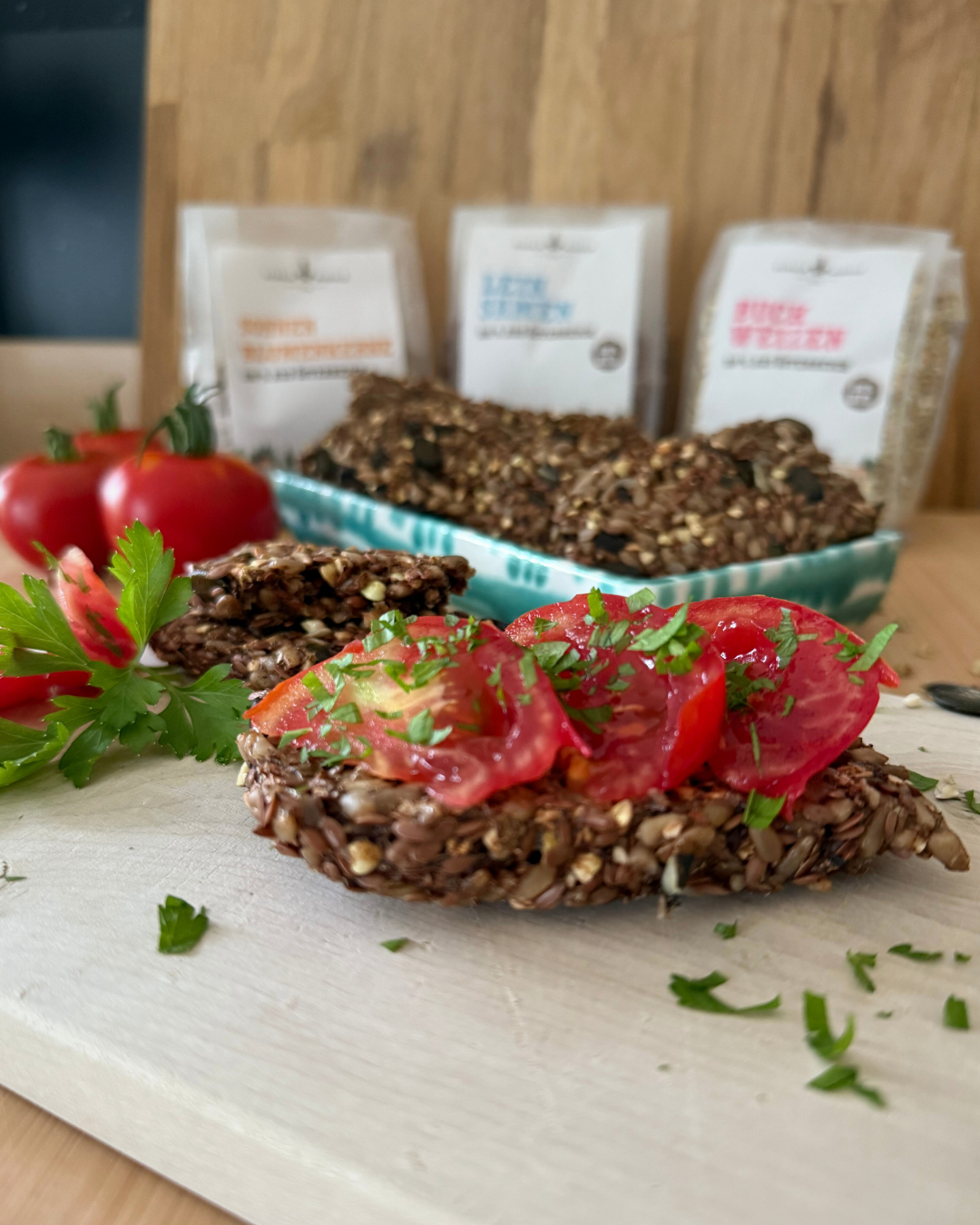 Saatenbrot-Scheibe mit Tomaten und Petersilie vor Schalk Mühle Saaten-Packungen