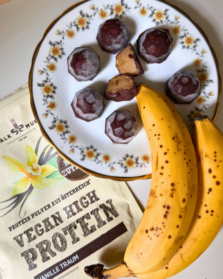 Schokolierte Bananenstücke auf einem Blumenteller mit Bananen neben Schalk Mühle Vegan High Protein Vanille Traum