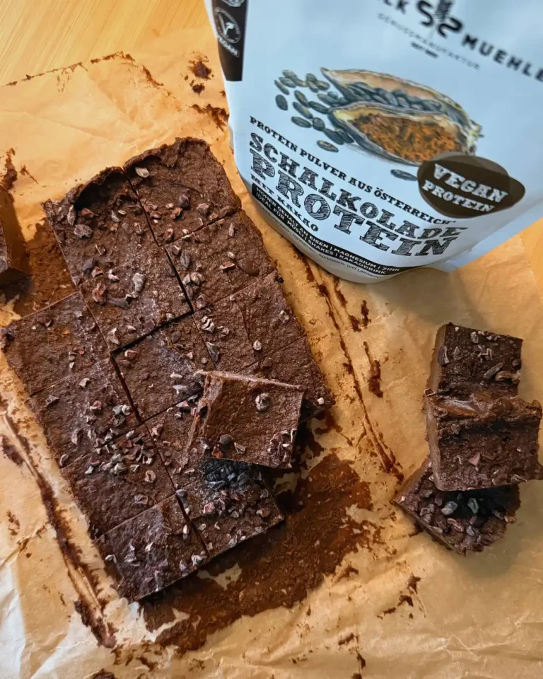 Schokoladen-Brownies mit Kakaonibs auf Backpapier neben Schalk Mühle Schalkolade Protein