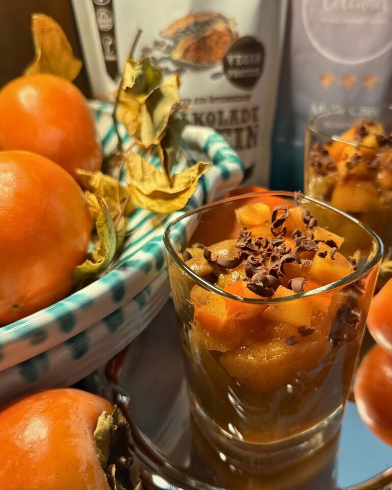 Kaki-Dessert im Glas mit Schokoraspeln, umgeben von frischen Kakis, neben Schalk Mühle Schalkolade Protein