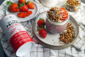 Strawberry Chia Pudding in a glass with granola and strawberries next to Schalk Mühle organic Vegan Protein Strawberry