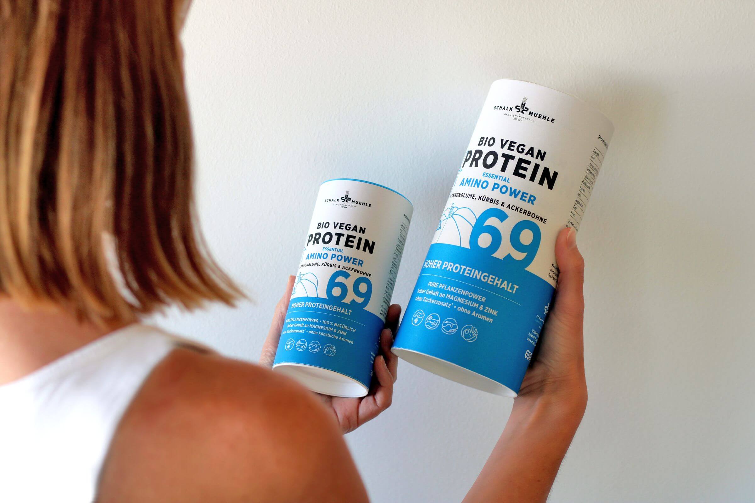 Person hält zwei Dosen Bio Vegan Protein Amino Power von Schalk Mühle mit 69 % Proteingehalt in den Händen.