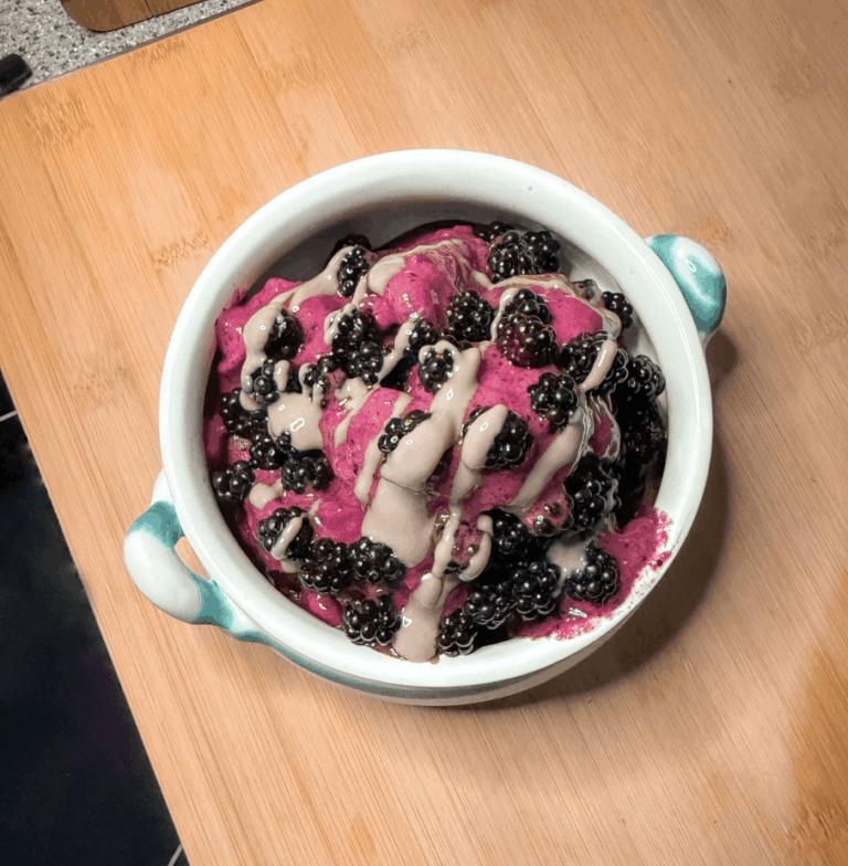 Beerige Nicecream mit Schalk Mühle Bio Multi Beeren Protein Mix , frischen Brombeeren und Bio Sonnenblumenkern Mus, in einer weißen Schüssel auf einem Tisch.