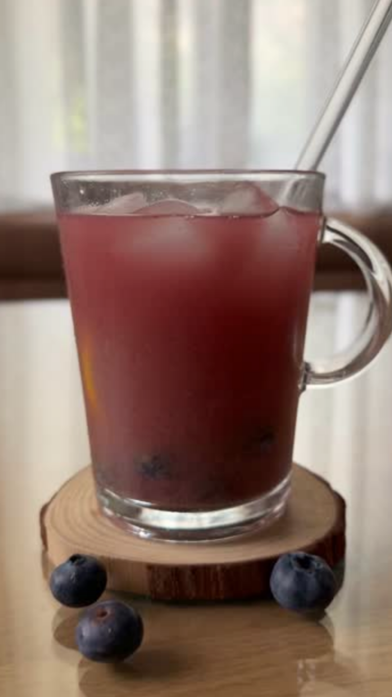 Dunkelrote Beeren-Limonade im Glas mit Eiswürfeln und frischen Heidelbeeren