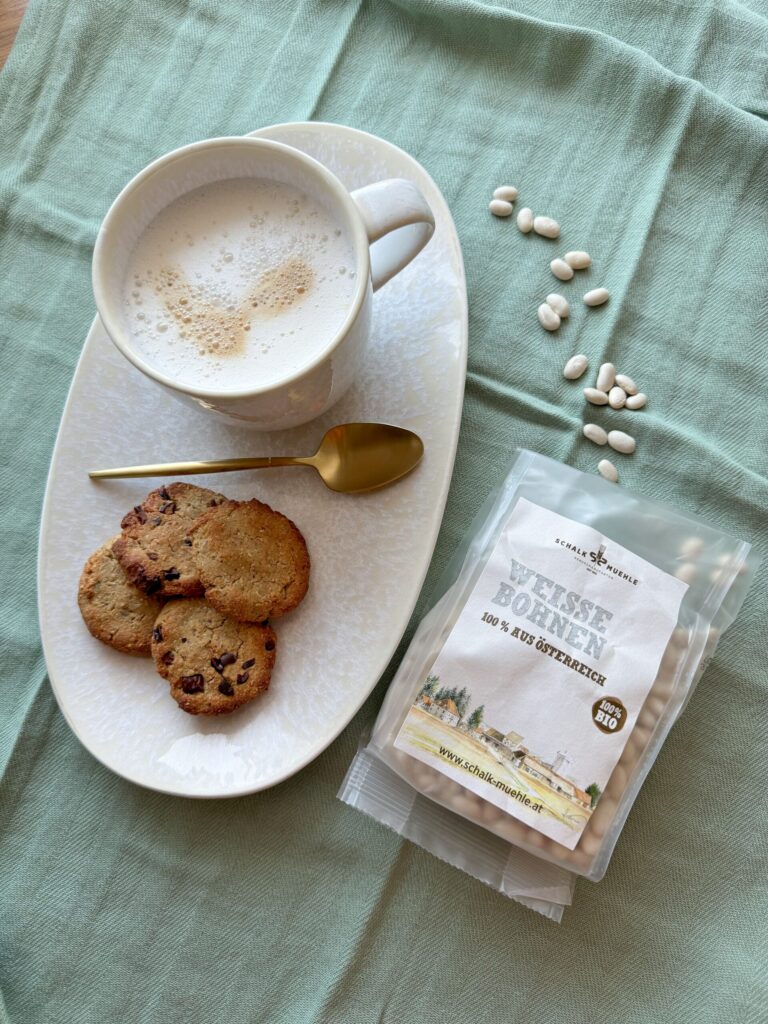 Weiße-Bohnen-Cookies mit Schokostückchen und Milchkaffee, daneben Schalk Mühle Weiße Bohnen