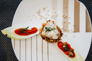 Buchweizen-Laibchen mit geschmolzenem Käse, Chicorée und Tomatensauce, dekoriert mit Kürbiskernen