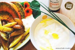 Geröstete Kürbisspalten und Kartoffeln mit Joghurt-Dip und Distelöl, dazu Schalk Mühle Distelöl-Flasche und Blüten