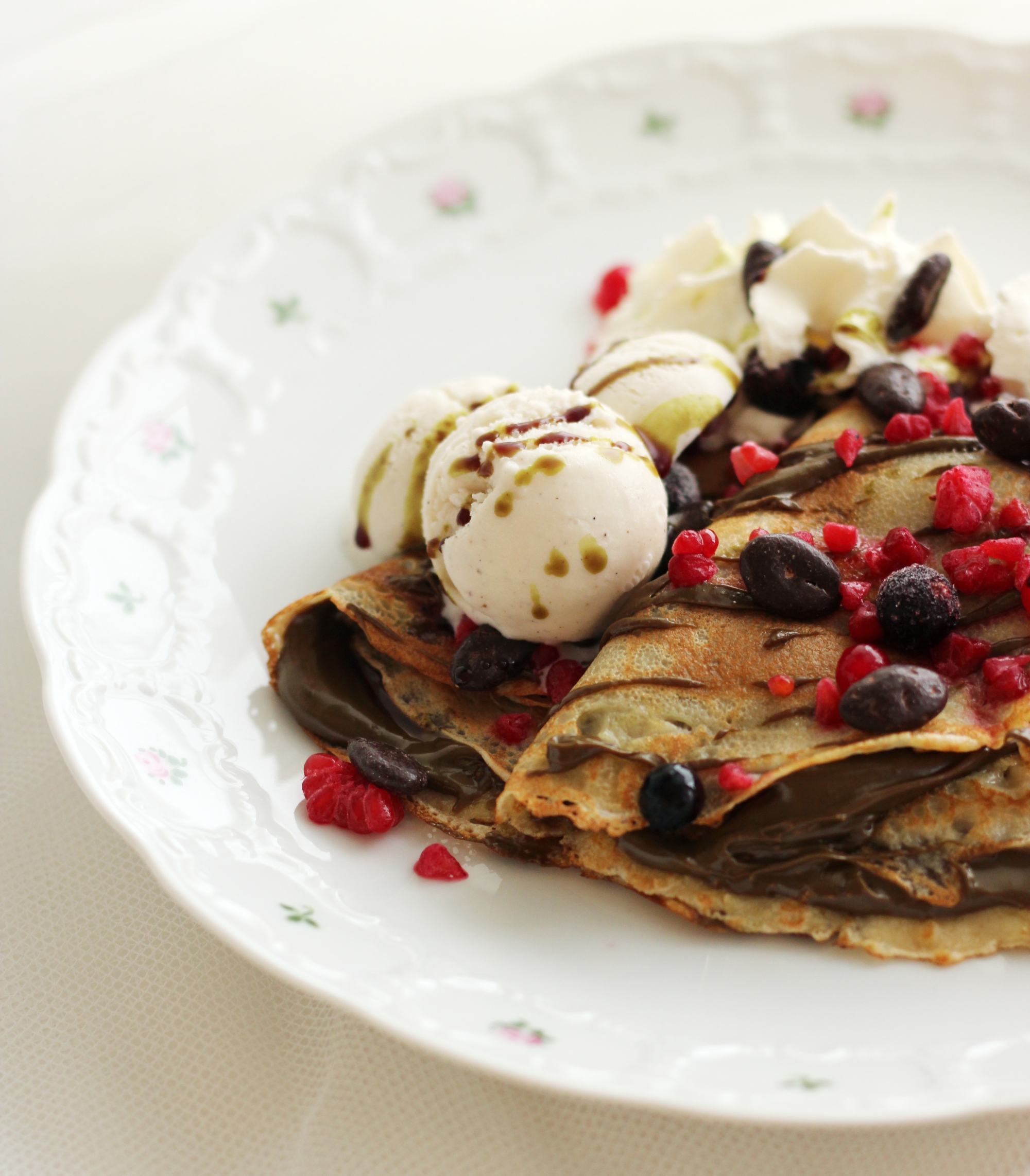 Palatschinke mit Schokocreme, Vanilleeis, Beeren und Kürbiskernen, beträufelt mit Kürbiskernöl auf Blümchenteller