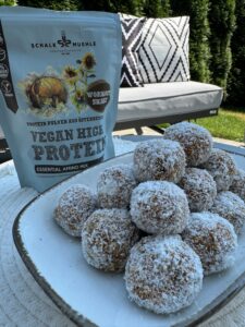 Vegane Kokos-Energiekugeln auf Teller im Garten, daneben Schalk Mühle Vegan High Protein