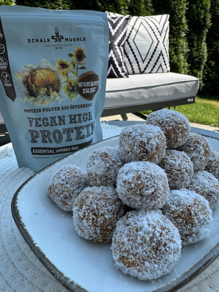 Vegane Kokos-Energiekugeln auf Teller im Garten, daneben Schalk Mühle Vegan High Protein