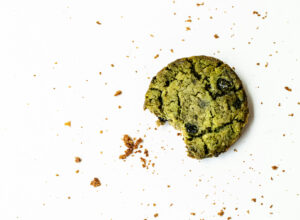 Angebissener grüner Matcha-Cookie mit Schokostücken und Krümeln auf hellem Untergrund