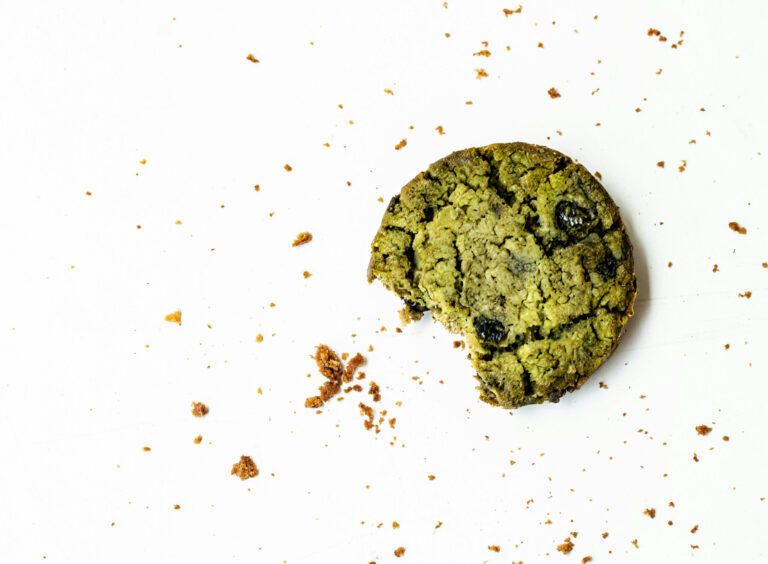 Angebissener grüner Matcha-Cookie mit Schokostücken und Krümeln auf hellem Untergrund