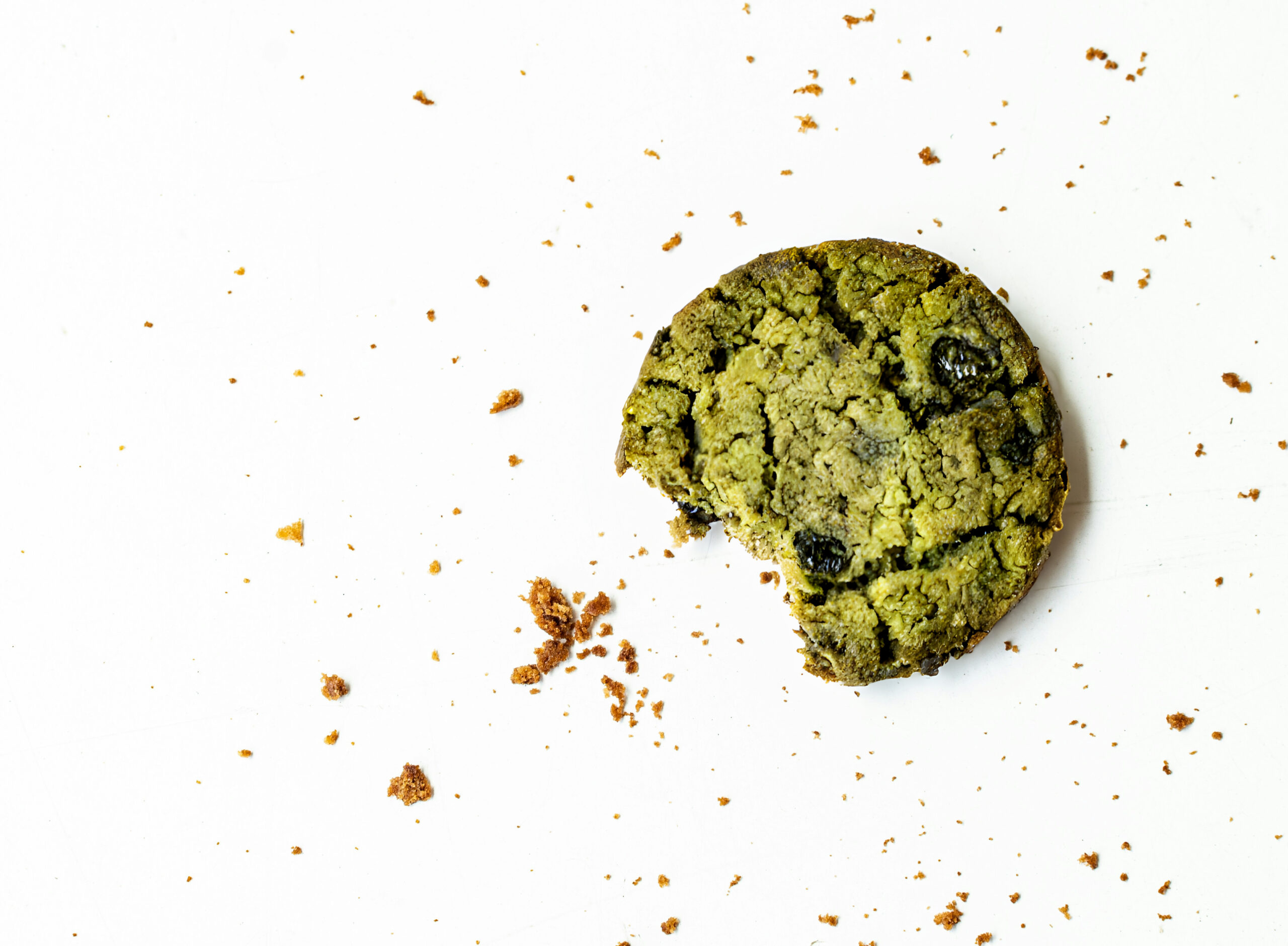 Angebissener grüner Matcha-Cookie mit Schokostücken und Krümeln auf hellem Untergrund