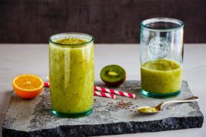 Grüner Smoothie mit Kiwi und Orange in zwei Gläsern auf einer Steinplatte