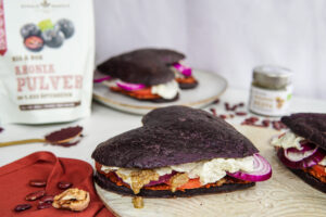 Herzförmiger Aronia-Burger mit Frischkäse, Tomate und roten Zwiebeln, daneben Schalk Mühle Aronia-Pulver