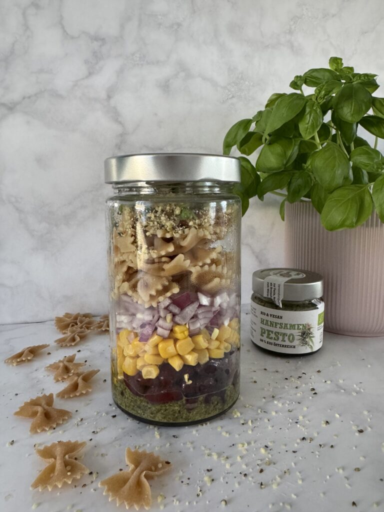 Geschichteter Meal-Prep-Nudelsalat im Glas mit Mais, Zwiebeln und Schalk Mühle Hanfsamen-Pesto