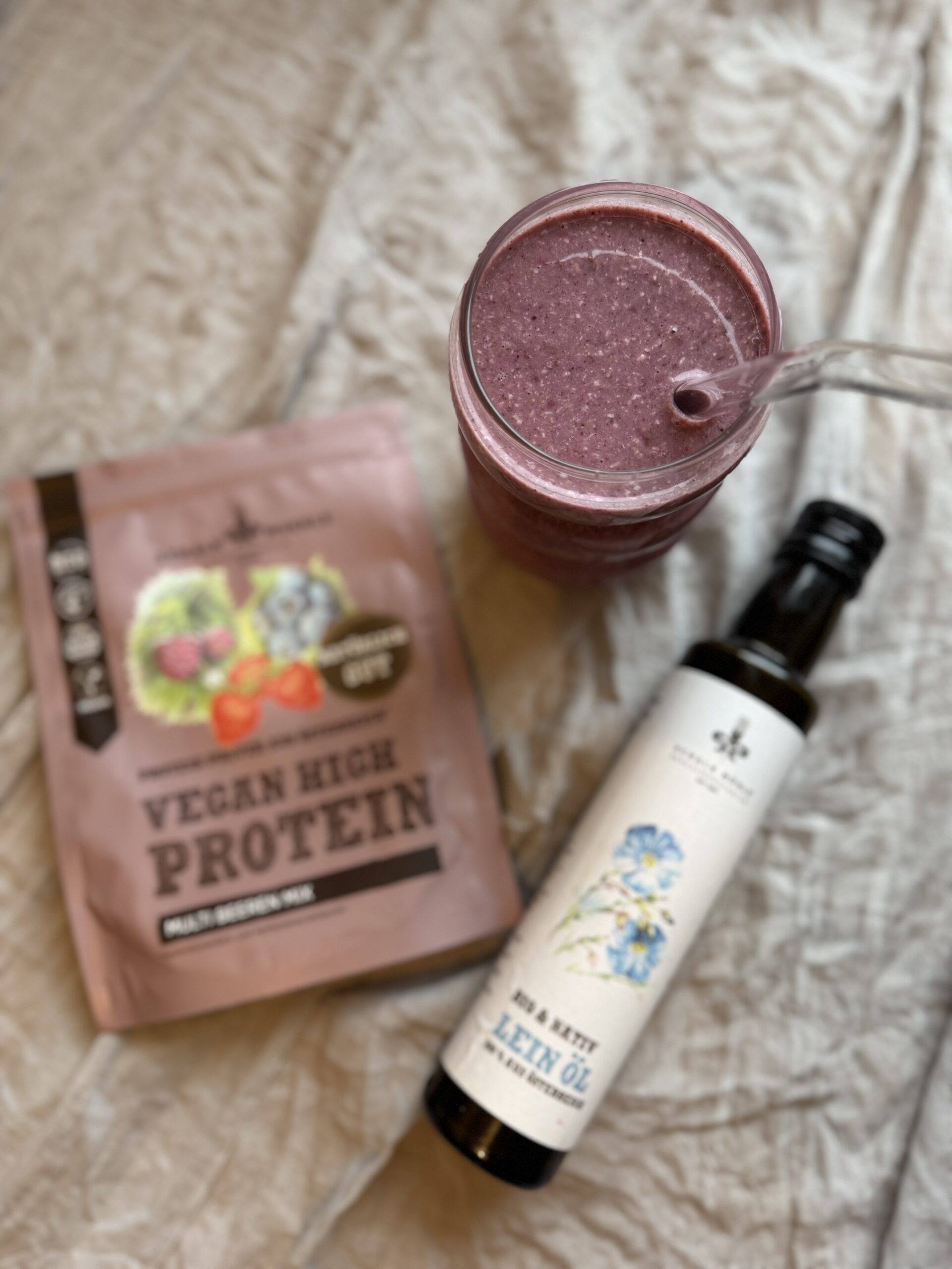 Rosafarbener Beeren-Shake im Glas mit Schalk Mühle Beeren-Proteinpulver und Leinöl