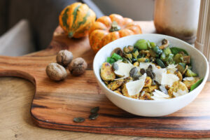 Kürbis-Gnocchi mit Zucchini, Kürbiskernen und Parmesan in einer Schale, dahinter Zierkürbisse und Walnüsse