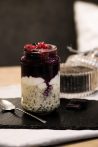 Overnight Oats mit Chiasamen, Beerenkompott und roten Ribiseln im Glas auf einer Schieferplatte