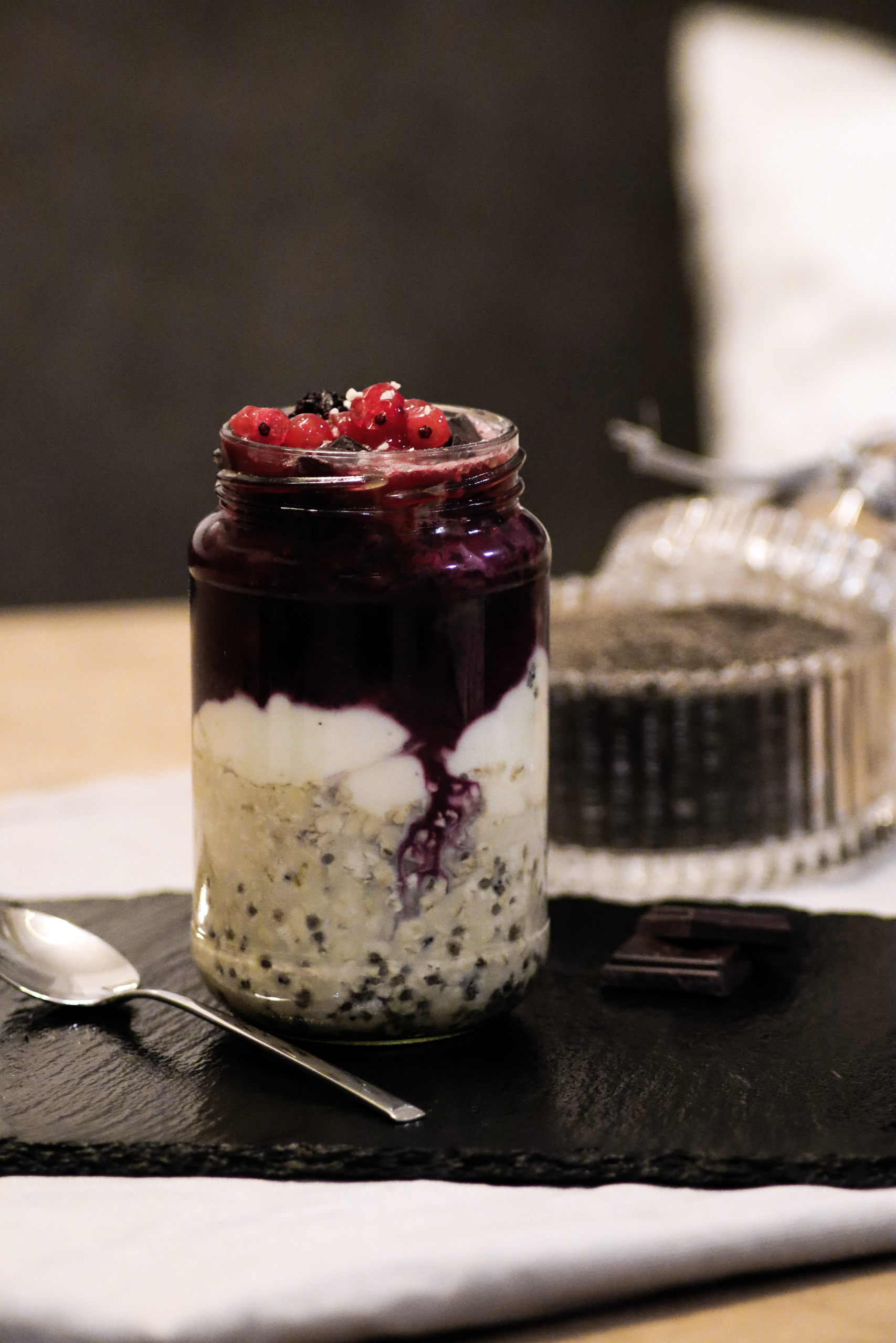 Overnight Oats mit Chiasamen, Beerenkompott und roten Ribiseln im Glas auf einer Schieferplatte