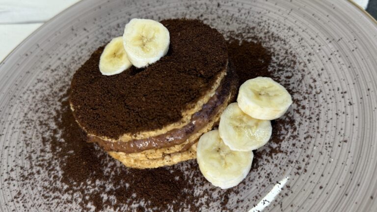 Herzförmige Pancakes mit Schokocreme, Kakao und Bananenscheiben auf Teller
