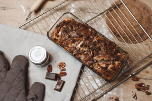 Schoko-Pekannuss-Kuchen in Glasform auf einem Kuchengitter, daneben Pekannüsse und Schokolade