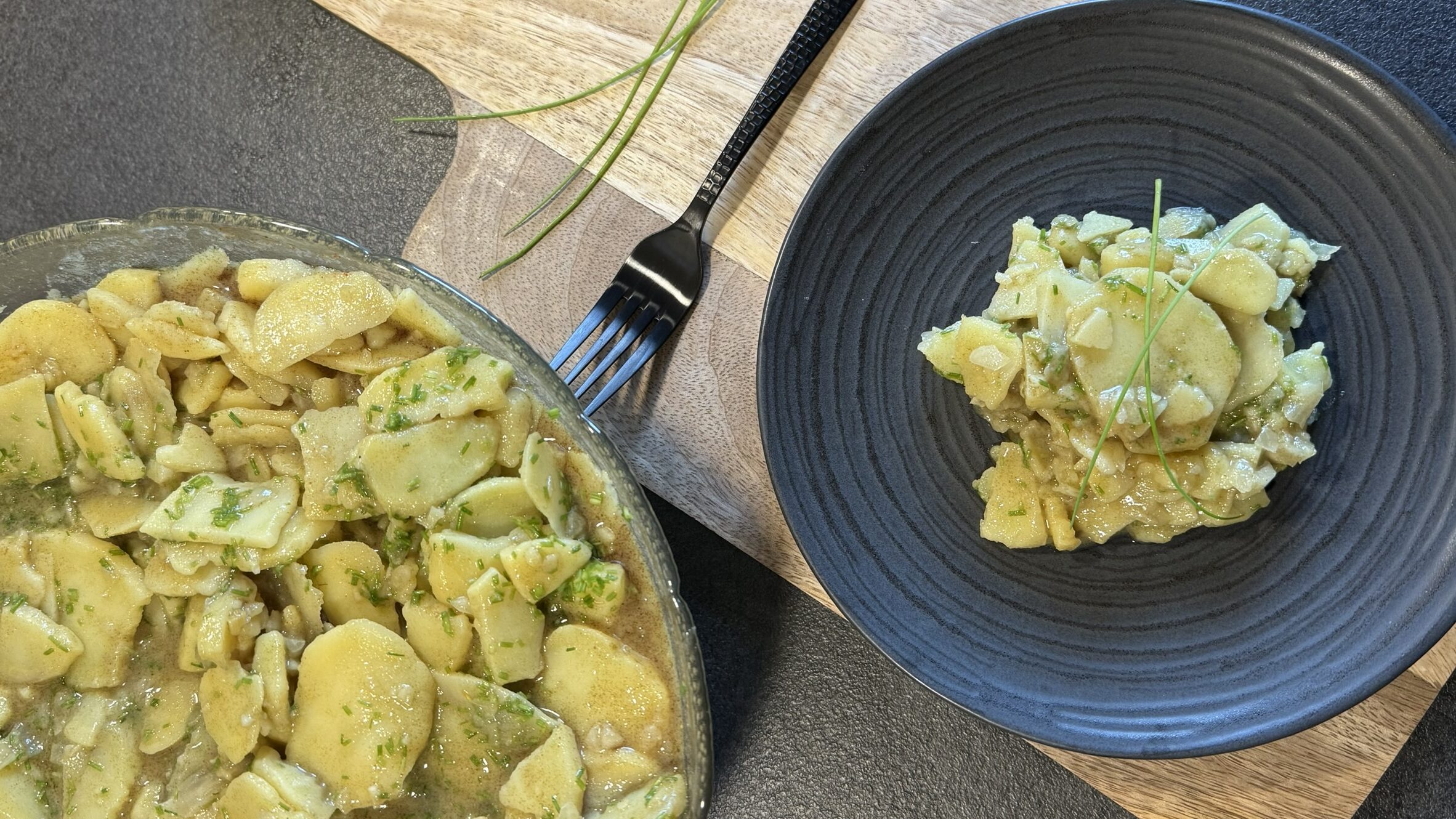Steirischer Erdäpfelsalat mit Schnittlauch in Schale und auf Teller mit Gabel