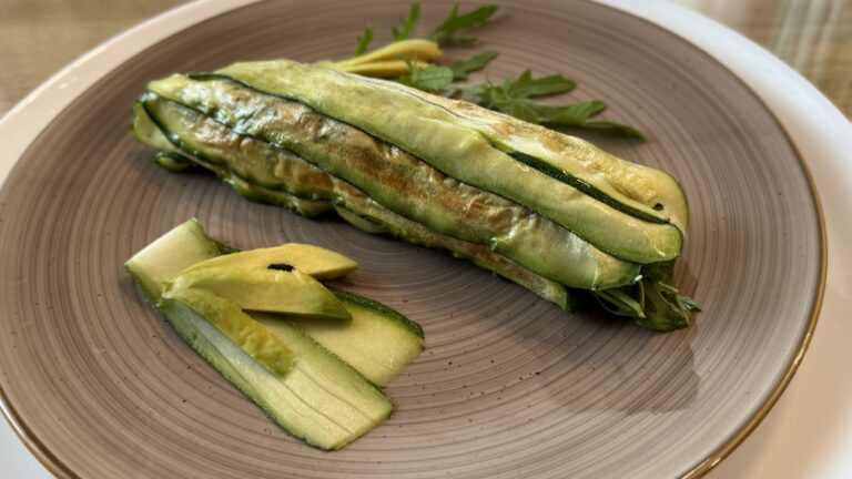 Zucchini-Rolle auf Teller mit Avocado und dünnen Zucchinischeiben
