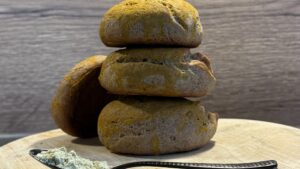 Gestapelte goldgelbe Kurkuma-Brötchen auf Holzbrett mit einem Löffel Proteinpulver
