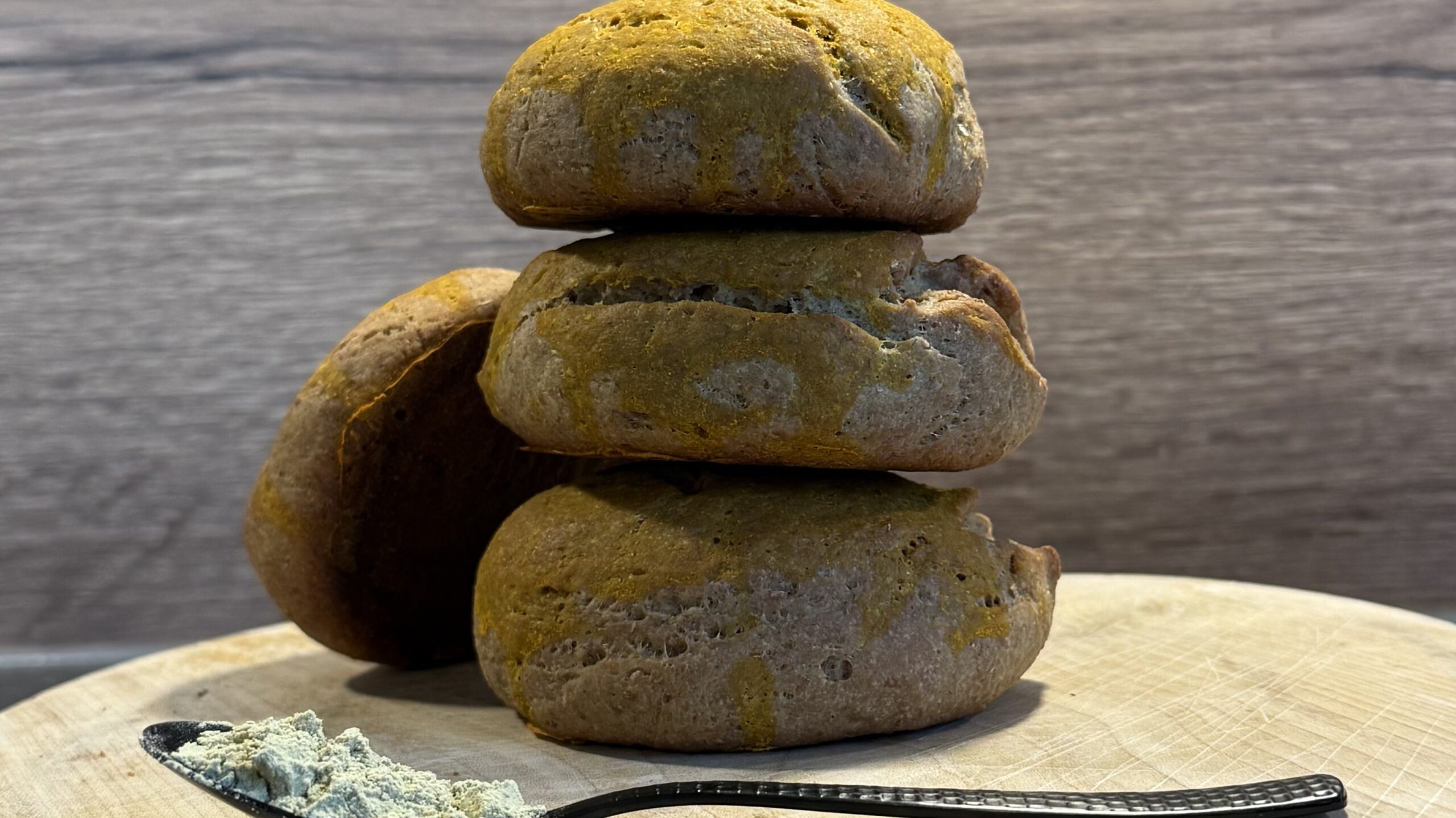 Gestapelte goldgelbe Kurkuma-Brötchen auf Holzbrett mit einem Löffel Proteinpulver