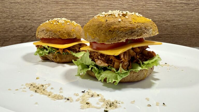 Zwei Pulled-Jackfruit-Burger mit Käse, Tomate und Salat auf goldgelben Buns mit Hanfsamen