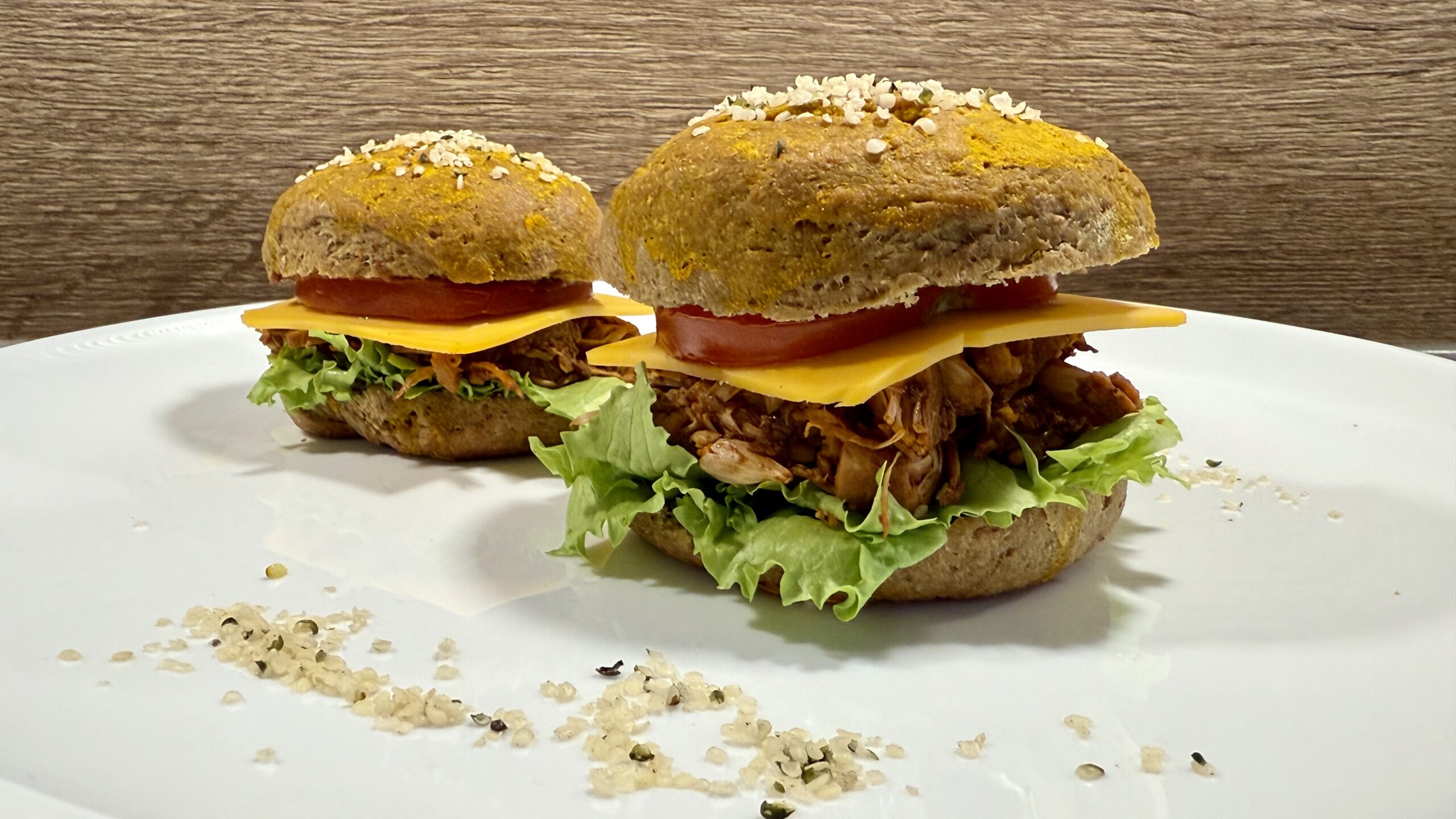 Zwei Pulled-Jackfruit-Burger mit Käse, Tomate und Salat auf goldgelben Buns mit Hanfsamen