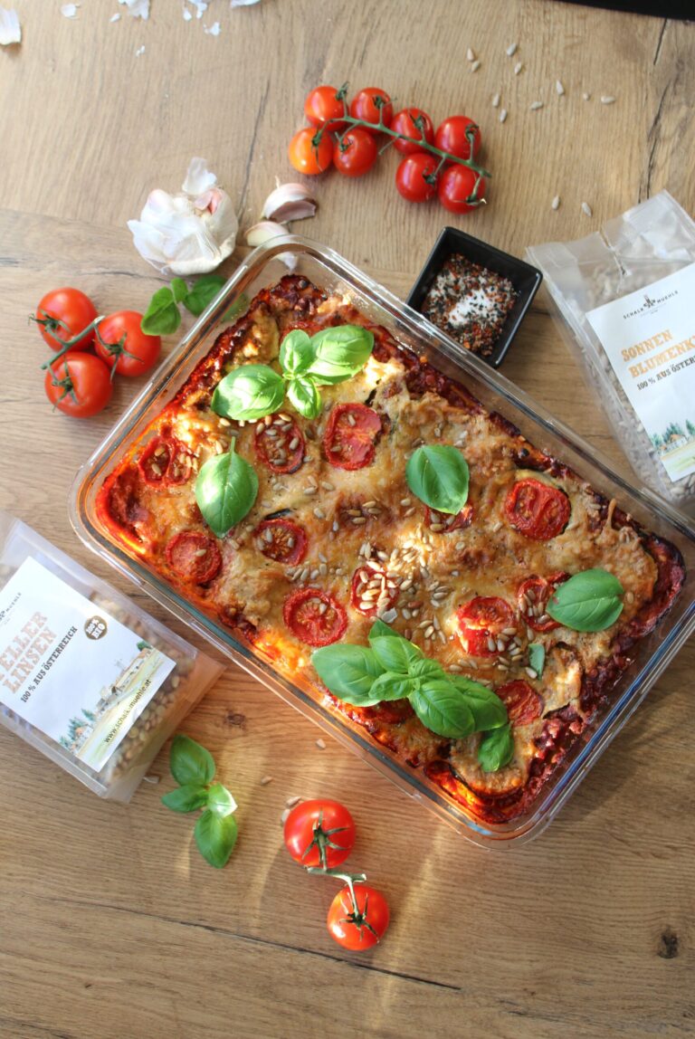 Gemüseauflauf mit Tomaten, Basilikum und Sonnenblumenkernen in Glasform, daneben Schalk Mühle Tellerlinsen und Sonnenblumenkerne