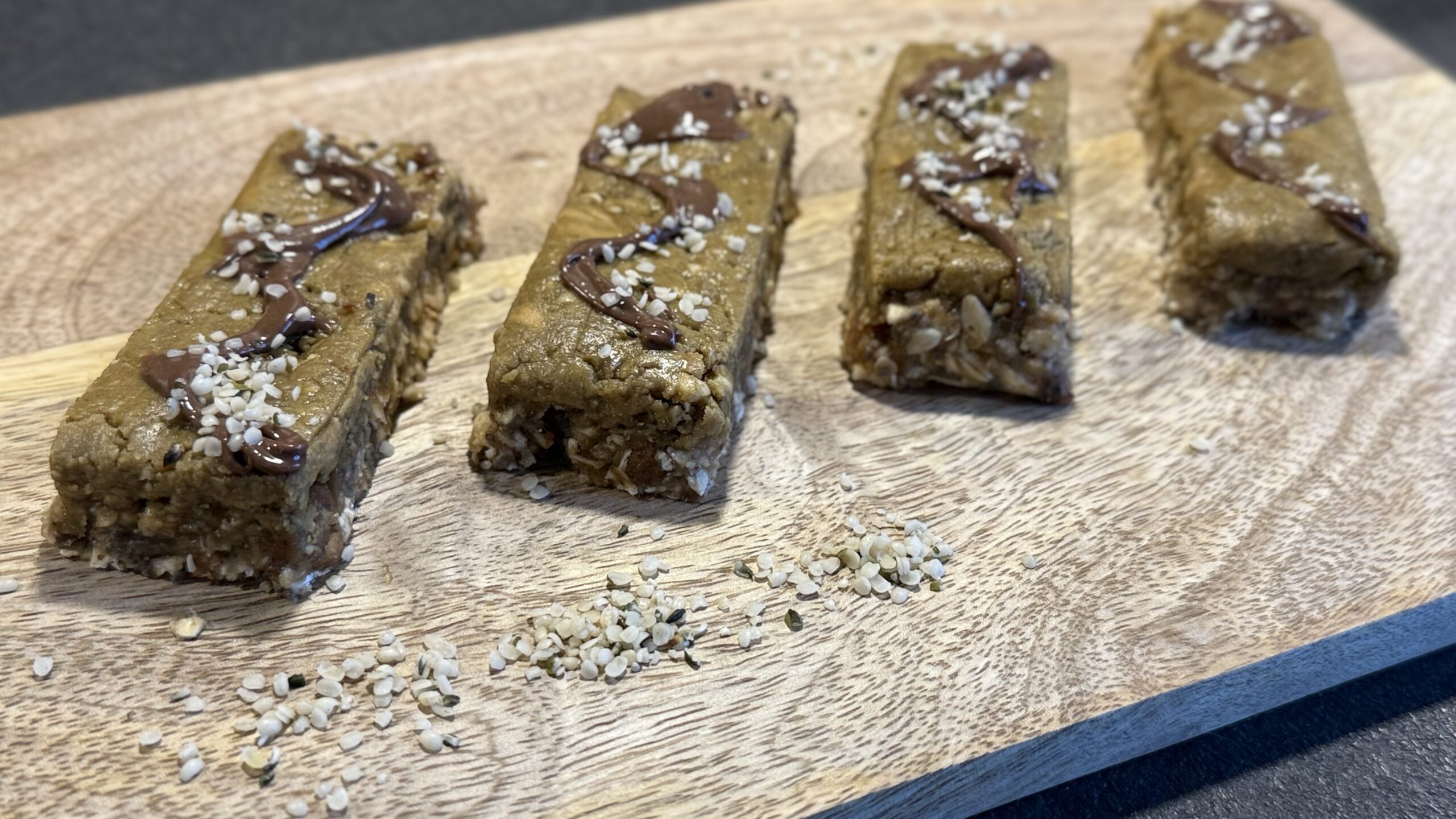 Vier selbstgemachte Proteinriegel mit Schokolade und Hanfsamen auf Holzbrett