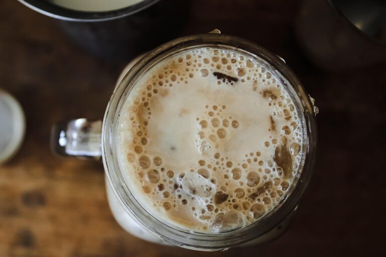 Eiskalter Protein-Schokoladen-Drink mit Milchschaum und Eiswürfeln im Glas von oben