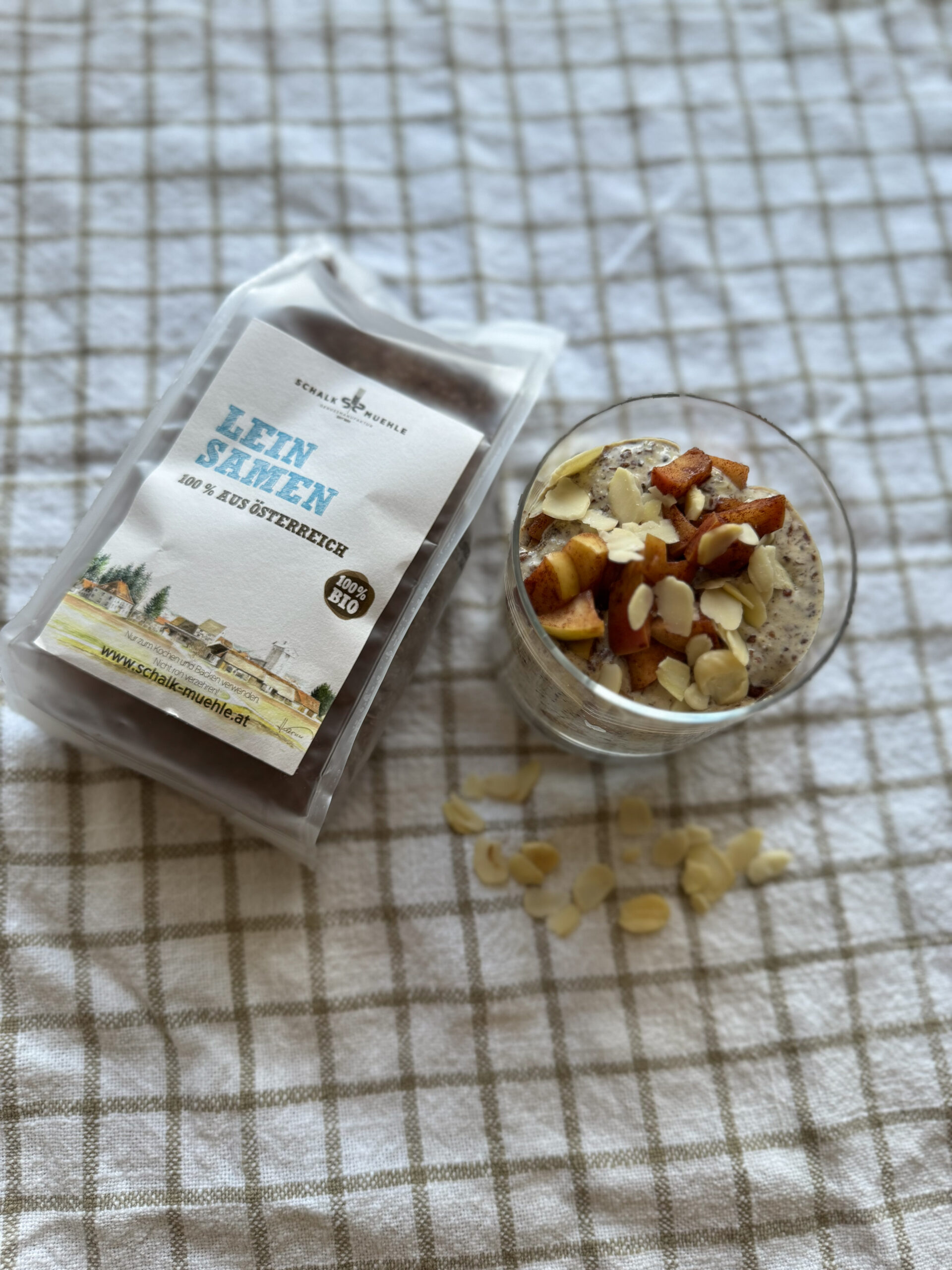 Leinsamen-Pudding im Glas mit Zimtapfel und Mandelblättchen, daneben Schalk Mühle Leinsamen