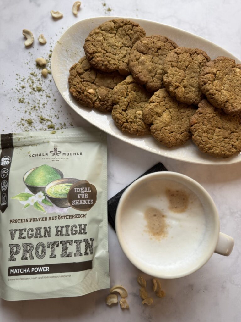 Matcha-Cookies auf Teller mit Schalk Mühle Matcha-Proteinpulver, Cappuccino und Cashewkernen