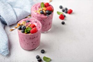 Beeren-Shake in zwei Gläsern, garniert mit Heidelbeeren, Himbeeren, Müsli und Minze