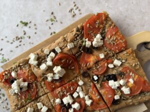 Fladenbrot mit Tomaten, Feta, Oliven und Sonnenblumenkernen in Stücke geschnitten auf Holzbrett