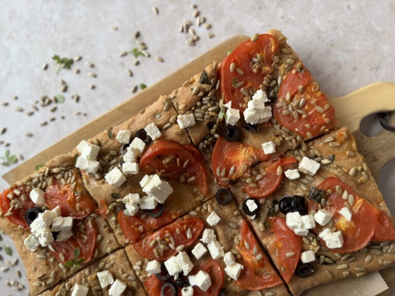 Fladenbrot mit Tomaten, Feta, Oliven und Sonnenblumenkernen in Stücke geschnitten auf Holzbrett